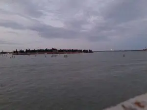 Real photograph of San Michele cemetery island across the Venetian lagoon at dusk, where Venice's temporary votive bridge sometimes connects to Fondamente Nove