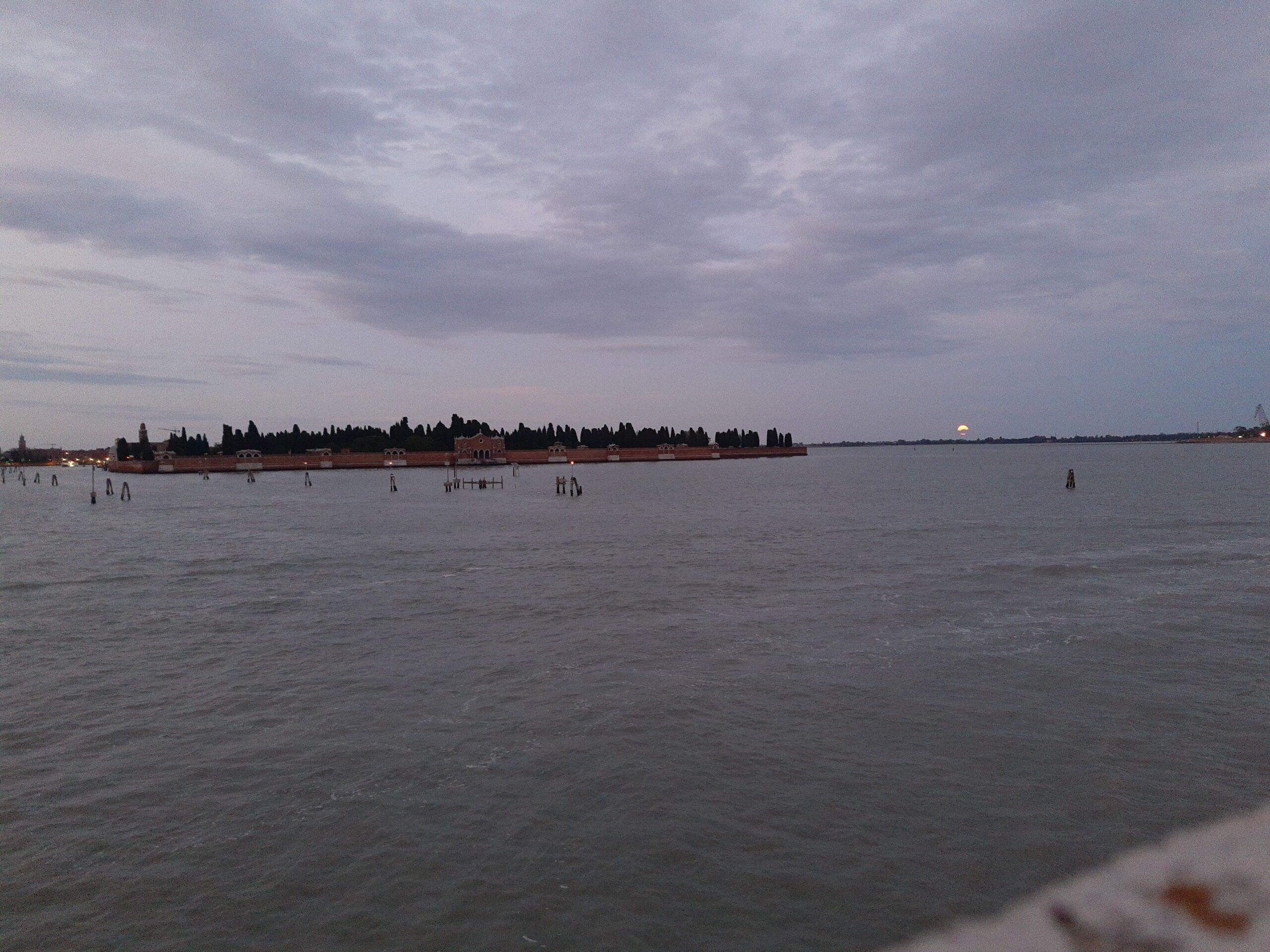 Real photograph of San Michele cemetery island across the Venetian lagoon at dusk, where Venice's temporary votive bridge sometimes connects to Fondamente Nove