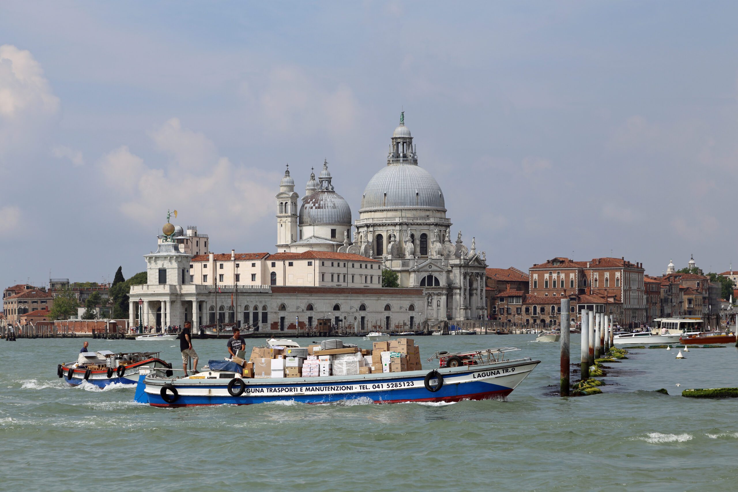 Real photograph of a freight transport boat carrying goods through Venice, illustrating the city's car-free logistics